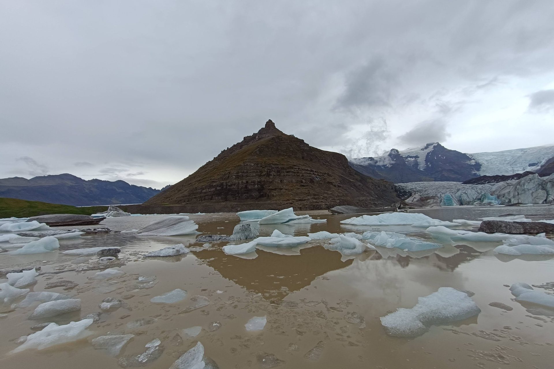 Laguna glaciar con una montaña piramidal al fondo, bloques de hielo varados y reflejo en el agua