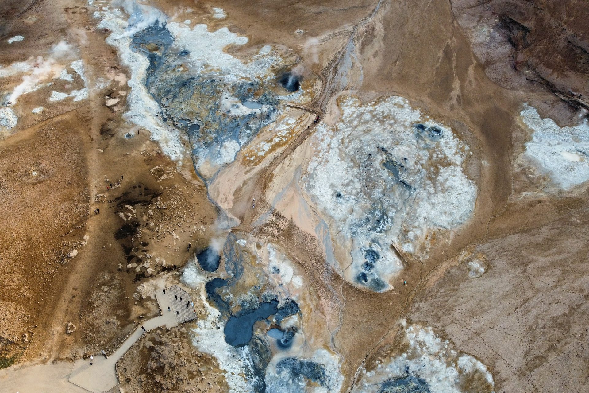 Vista cenital de un campo geotérmico con pozas azules y turquesas sobre tierra ocre y costras blancas