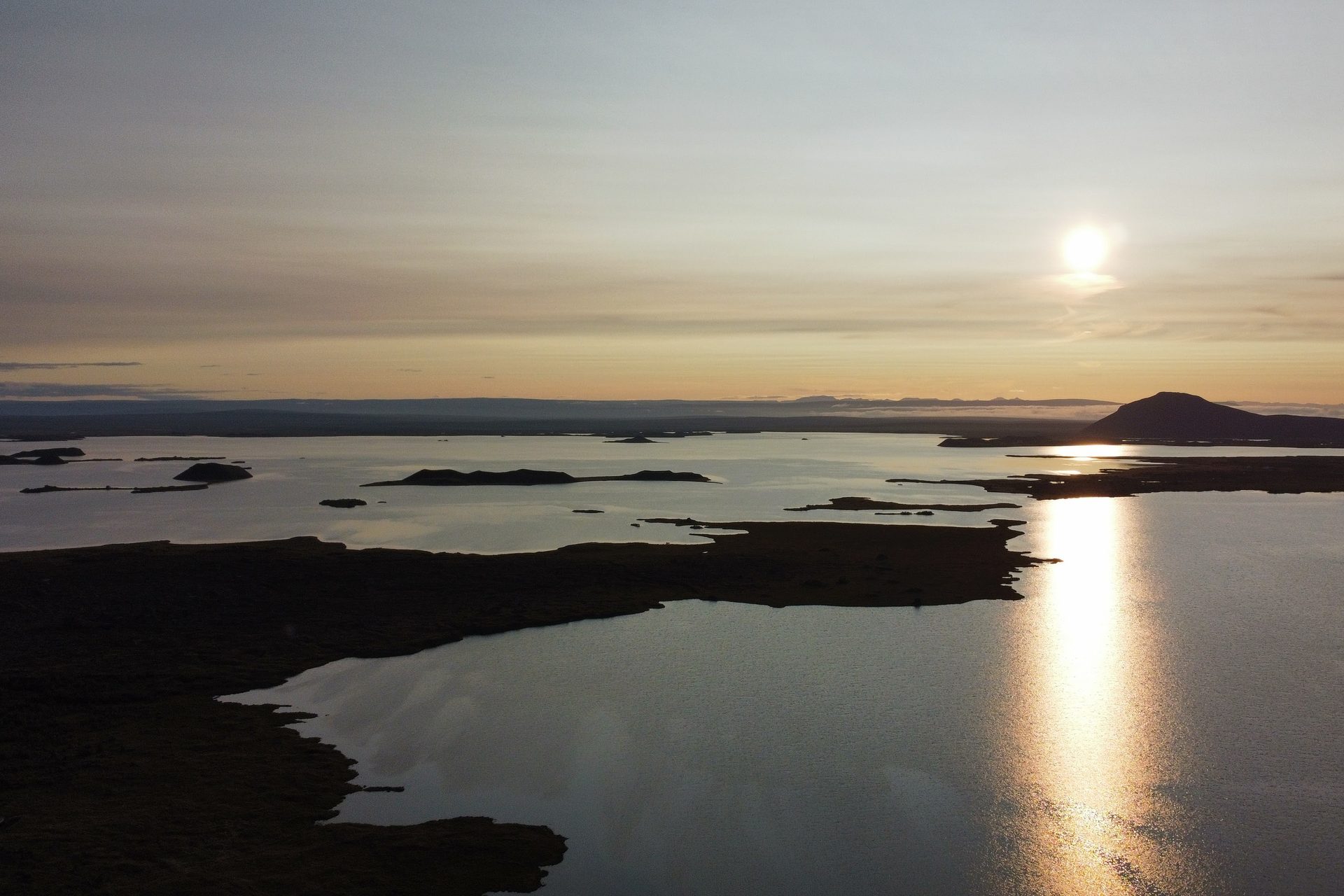 Puesta de sol sobre un lago con penínsulas oscuras y el reflejo del sol partiendo el agua en dos