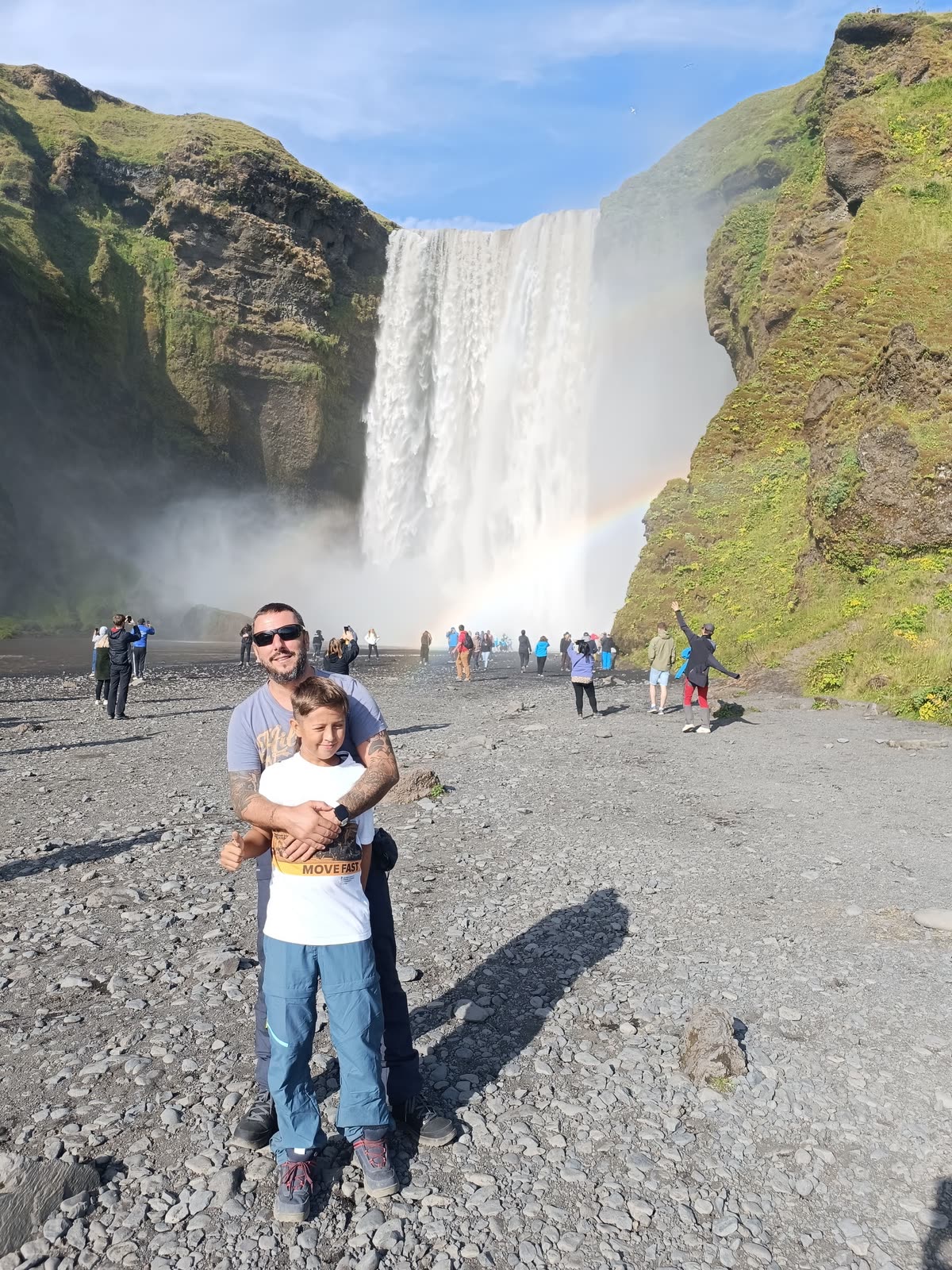 Dos personas ante una gran cascada, con un arcoíris en la bruma