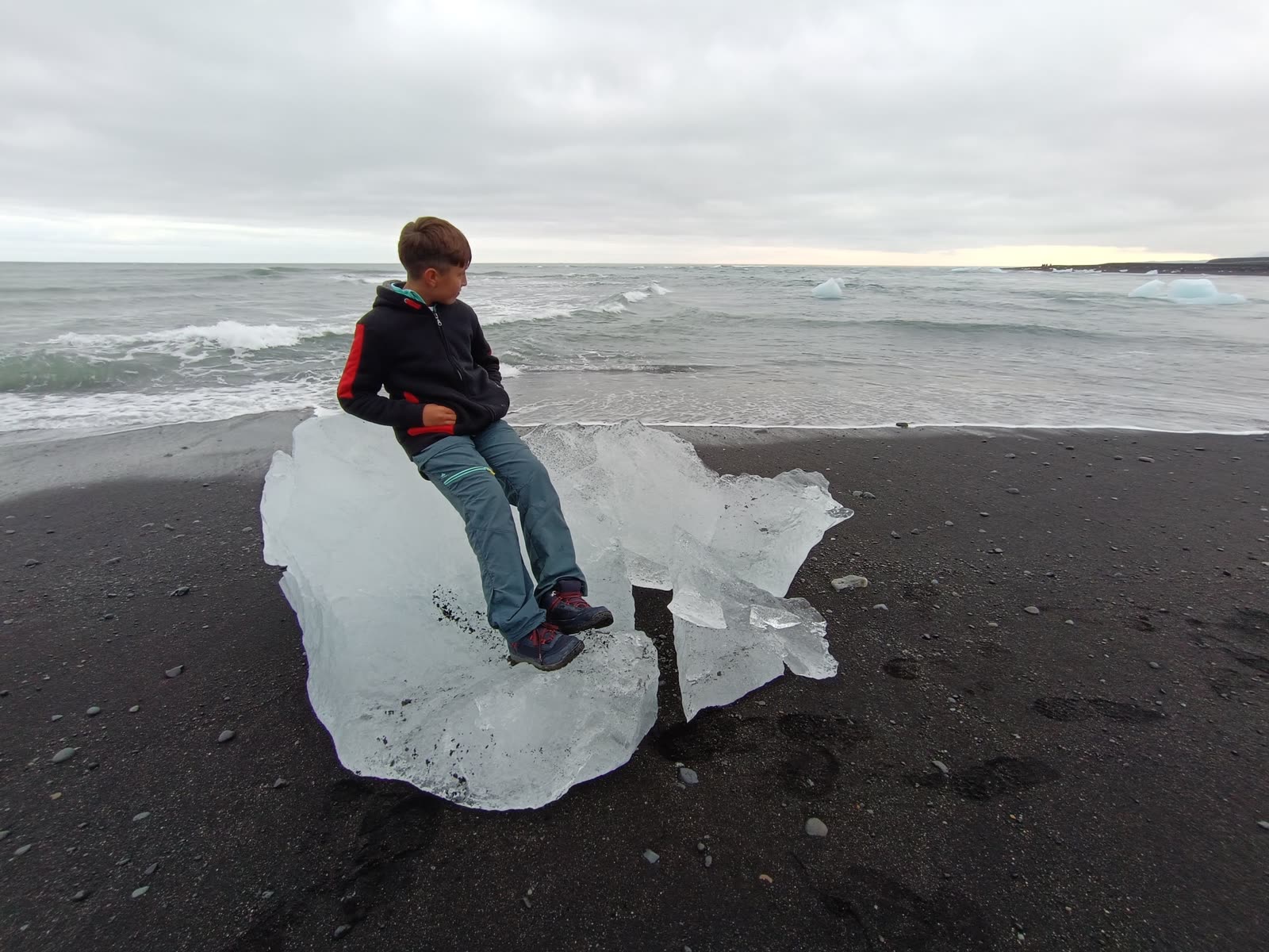 Niño sentado sobre un bloque de hielo en una playa de arena negra de Islandia